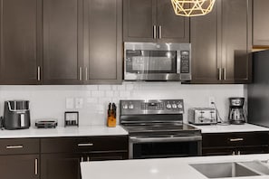 A modern kitchen with dark cabinets, stainless steel appliances, and a white countertop. - 2929 SS - Disney Delight: 4BR, Pool, Near Parks (Kissimmee)