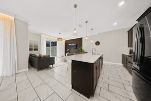 A modern kitchen with a central island, dark cabinetry, and a large refrigerator. - 2929 SS - Disney Delight: 4BR, Pool, Near Parks (Kissimmee)