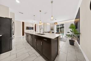 A modern kitchen with a central island, dark cabinetry, and a large refrigerator. - 2929 SS - Disney Delight: 4BR, Pool, Near Parks (Kissimmee)