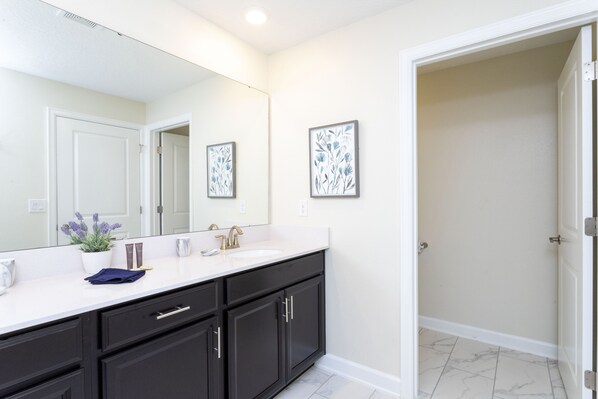 A bathroom with a white vanity, dark cabinets, a large mirror, and two framed floral artworks on the wall.