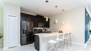 A modern kitchen with dark cabinets, stainless steel appliances, a white island with bar stools, and pendant lighting.