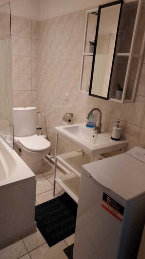 Un baño con inodoro, lavamanos, espejo y un refrigerador blanco.