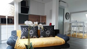 Un salon moderne avec un canapé, des coussins décoratifs, une plante et un coin repas comprenant une table et des chaises.