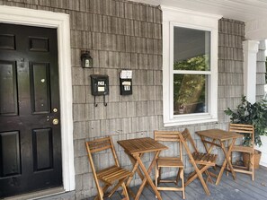 A porch with wooden chairs and tables, a black door, and mailbox numbers 1F and 2F.
