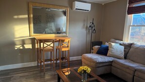 Ein Wohnzimmer mit einem Holztisch, einer Couch, einem Glastisch mit Blumen, einem Gemälde an der Wand und einer Klimaanlage.