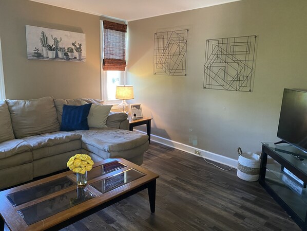 A living room with a sofa, coffee table, lamp, artwork, and a television.