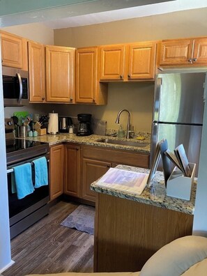 A kitchen with wooden cabinets, a stainless steel refrigerator, a microwave, a coffee maker, and a granite countertop.