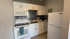 Une cuisine de taille réduite, avec des meubles blancs, un four à micro-ondes, une cuisinière et un réfrigérateur.