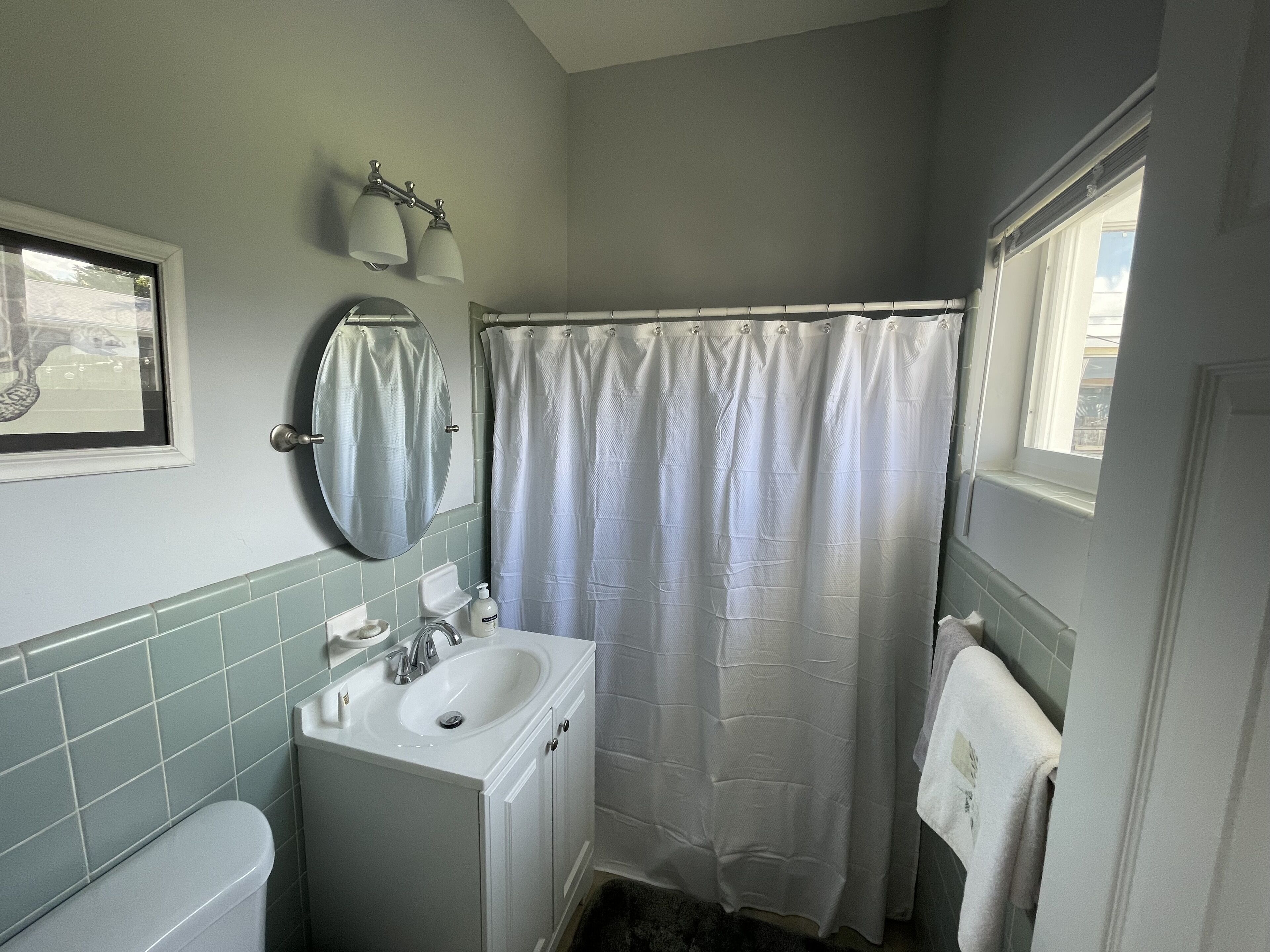 A bathroom with a white sink, mirror, and toilet, a shower curtain, and a window.