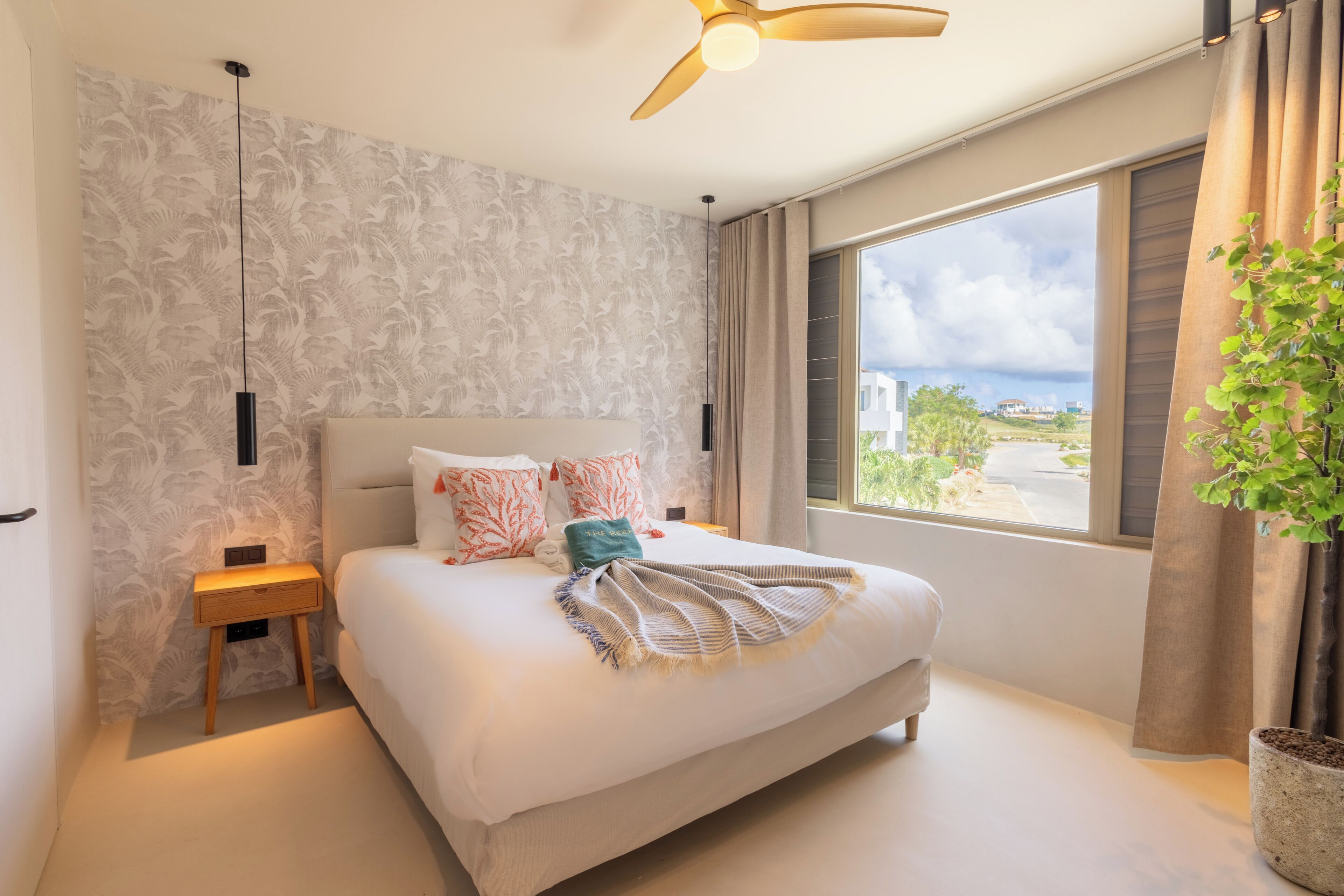 A bedroom with a bed, a nightstand, a ceiling fan, a window with curtains, and a potted plant.