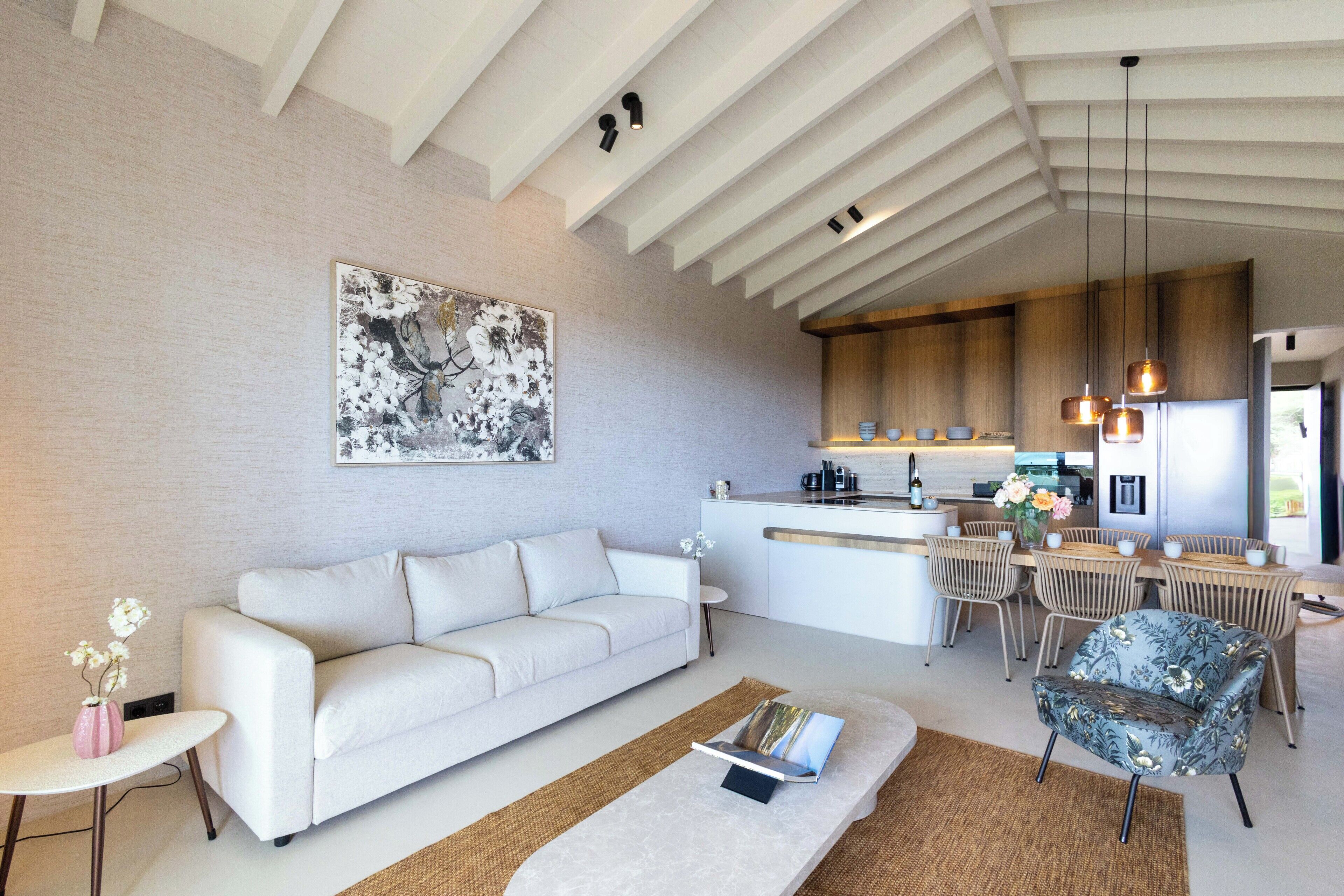 Una sala de estar moderna con sofá, mesa de centro y comedor con sillas, con cocina al fondo.