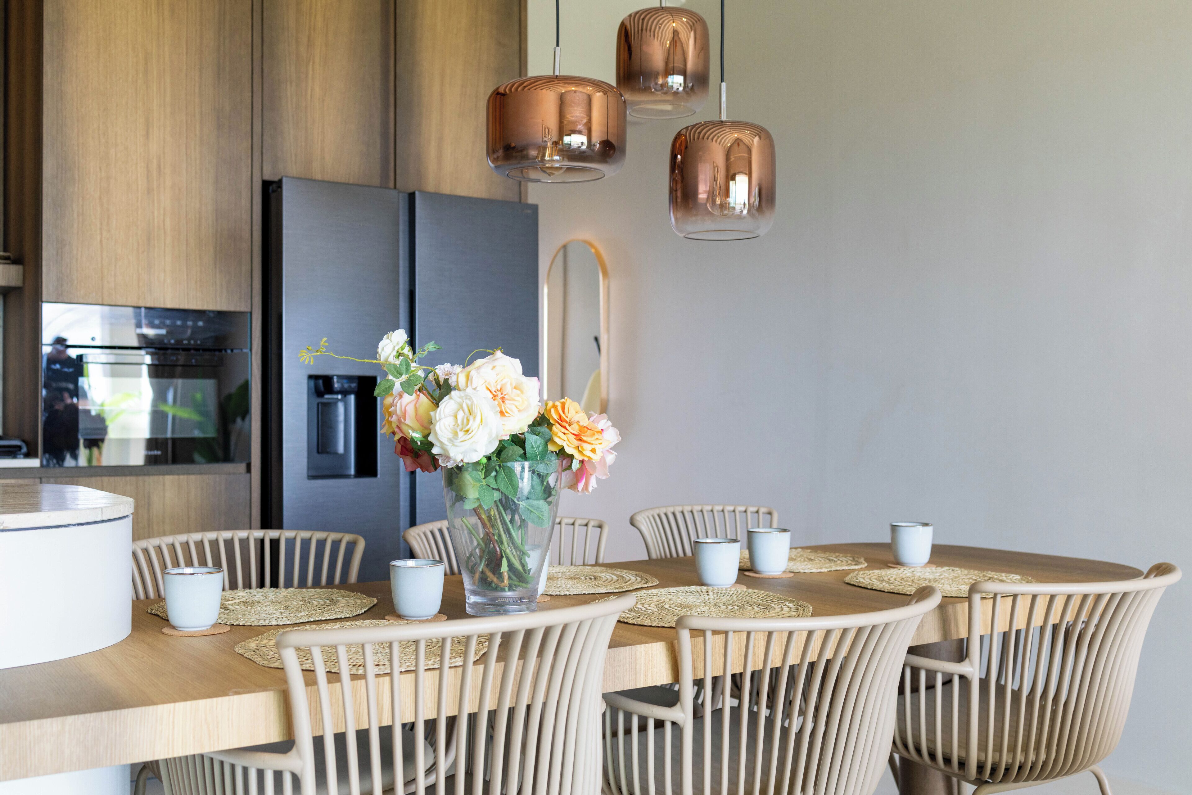 A modern kitchen with a dining area, featuring a stainless steel refrigerator, wooden cabinets, and a round table with chairs.