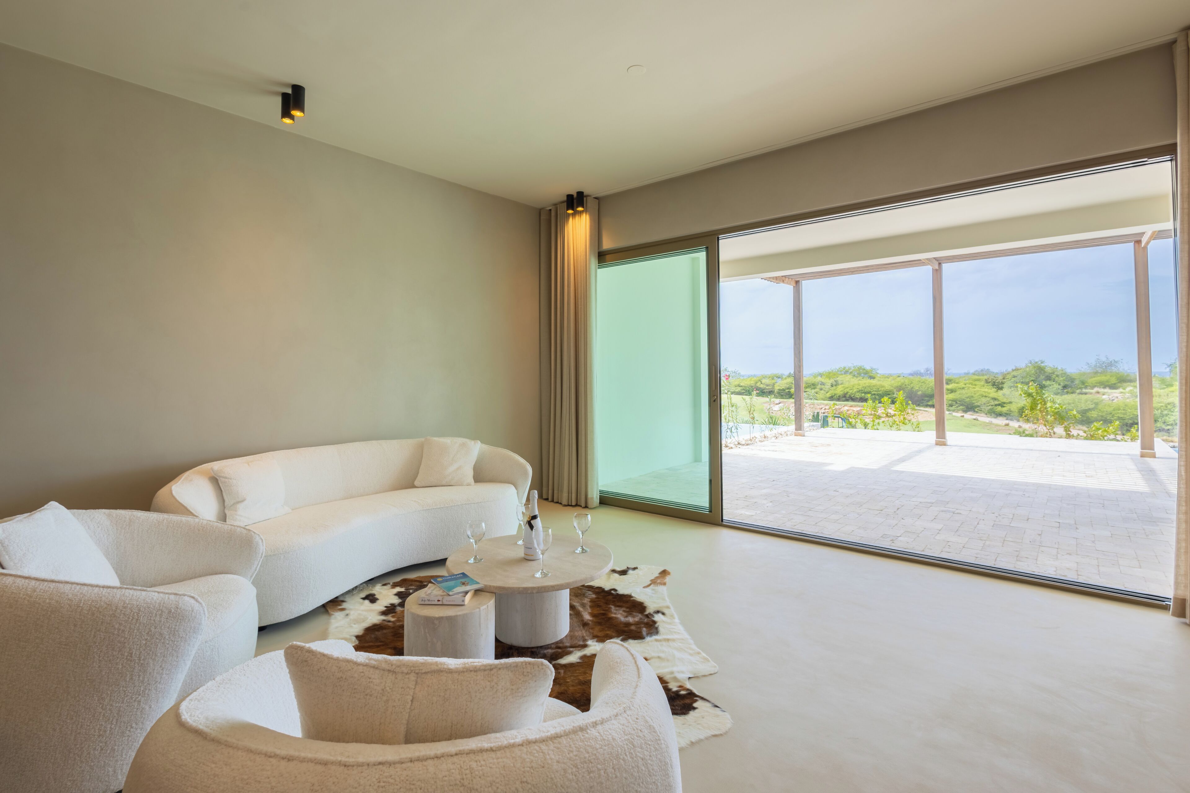 A modern living room with a white sofa, a round coffee table, and a large glass door leading to an outdoor patio.