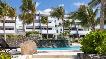 Un resort moderno con piscina, palmeras y un muro de piedra.