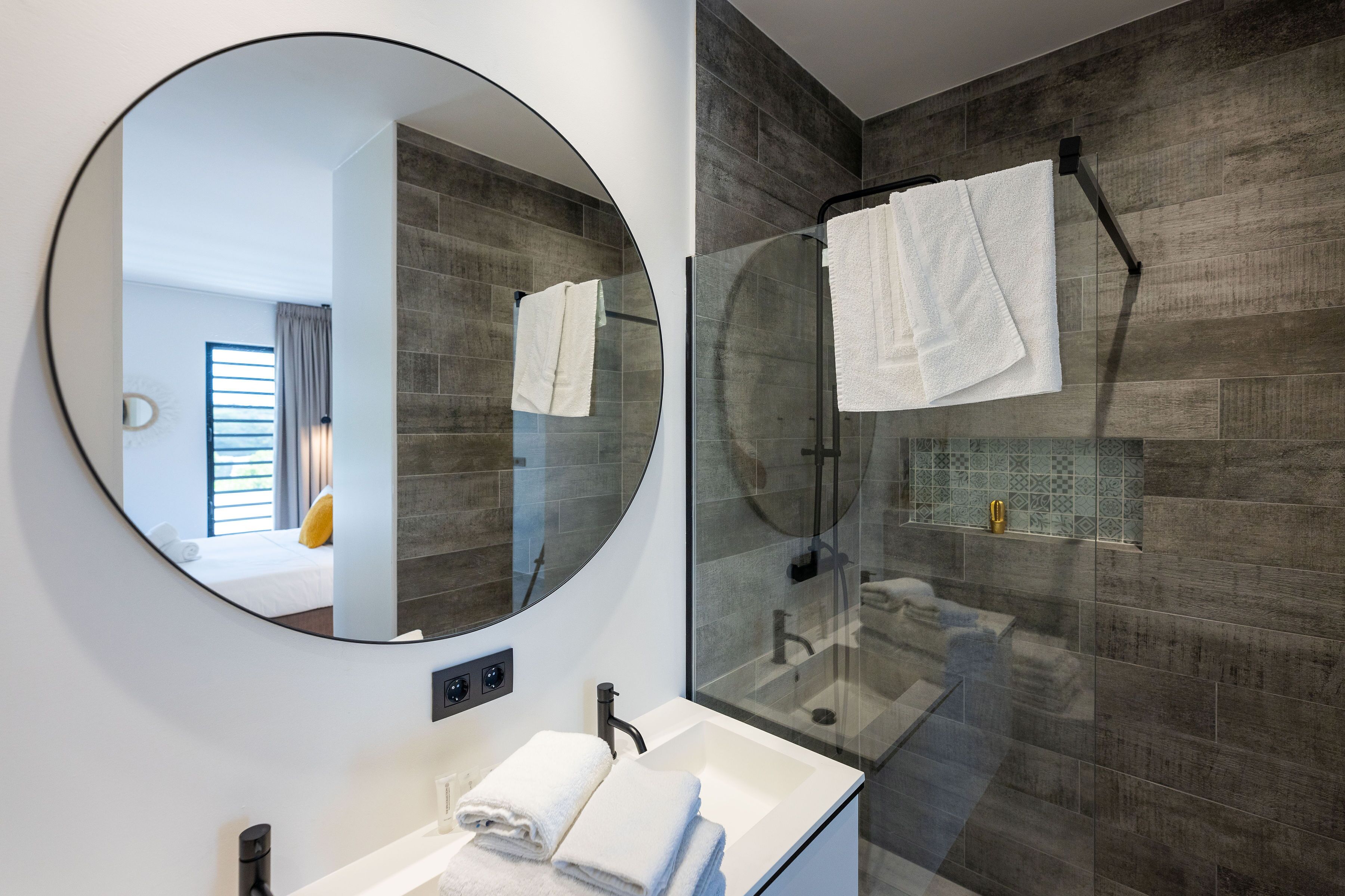 A modern bathroom with a round mirror, a glass-enclosed shower, and a white sink.