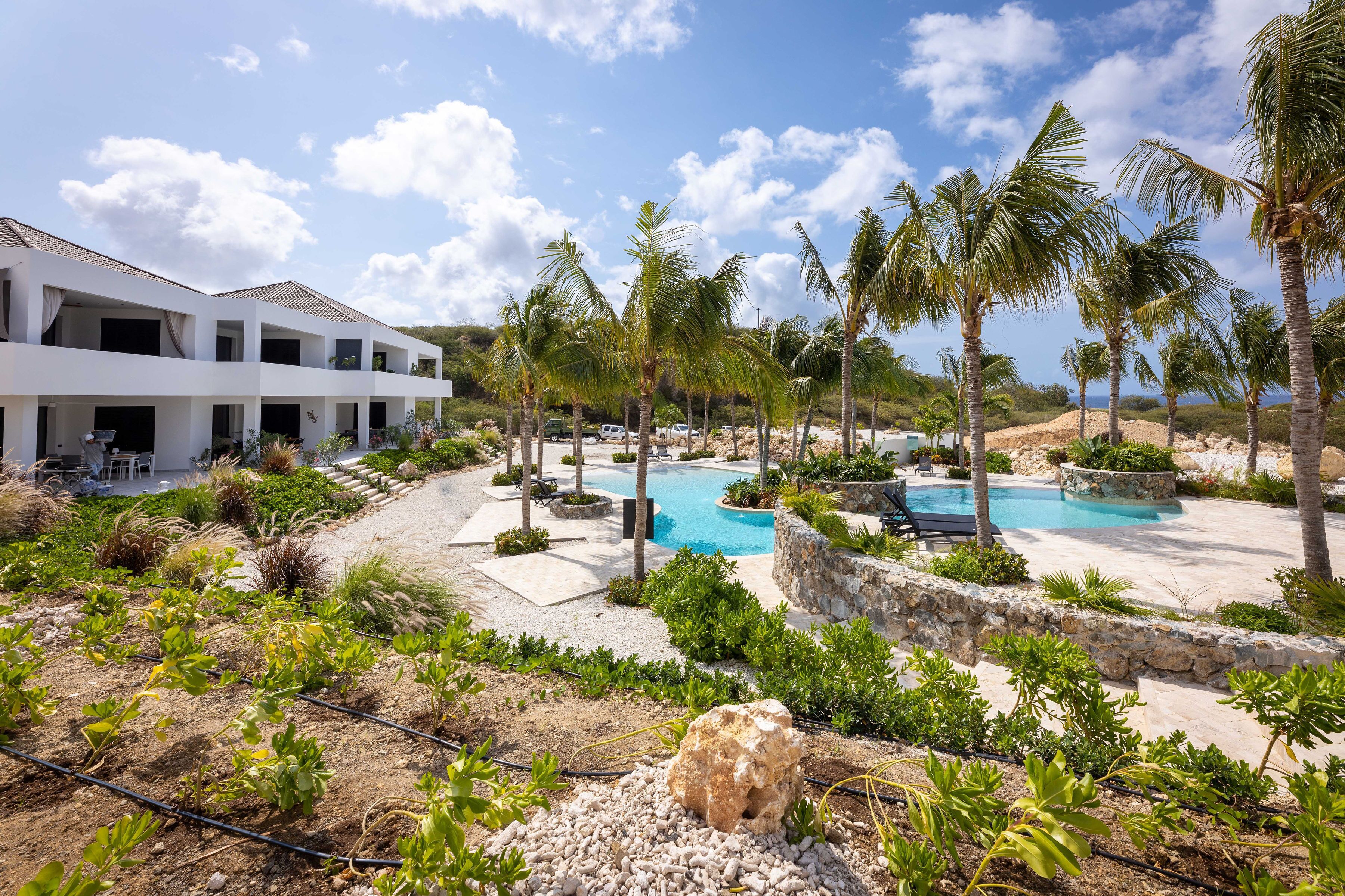 Ein Resort mit Pool, Palmen und einem weißen Gebäude mit Balkonen.
