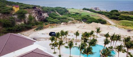 Een resort met een zwembad, palmbomen en uitzicht op de oceaan.