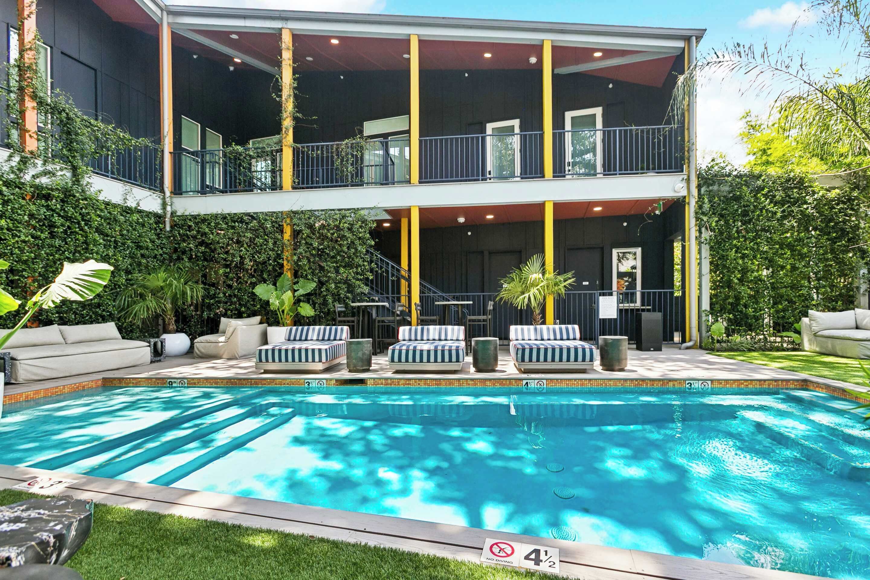 A two-story building with a swimming pool, outdoor seating, and a covered patio area.