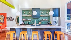 Una cocina moderna con una isla central, taburetes de bar y un ventanal amplio.