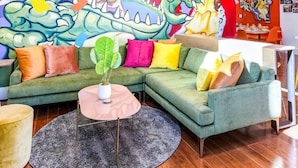 Un mural vibrante con un dragón, músicos y personajes festivos. Se ve un sofá verde, una mesa de centro redonda y un espejo.