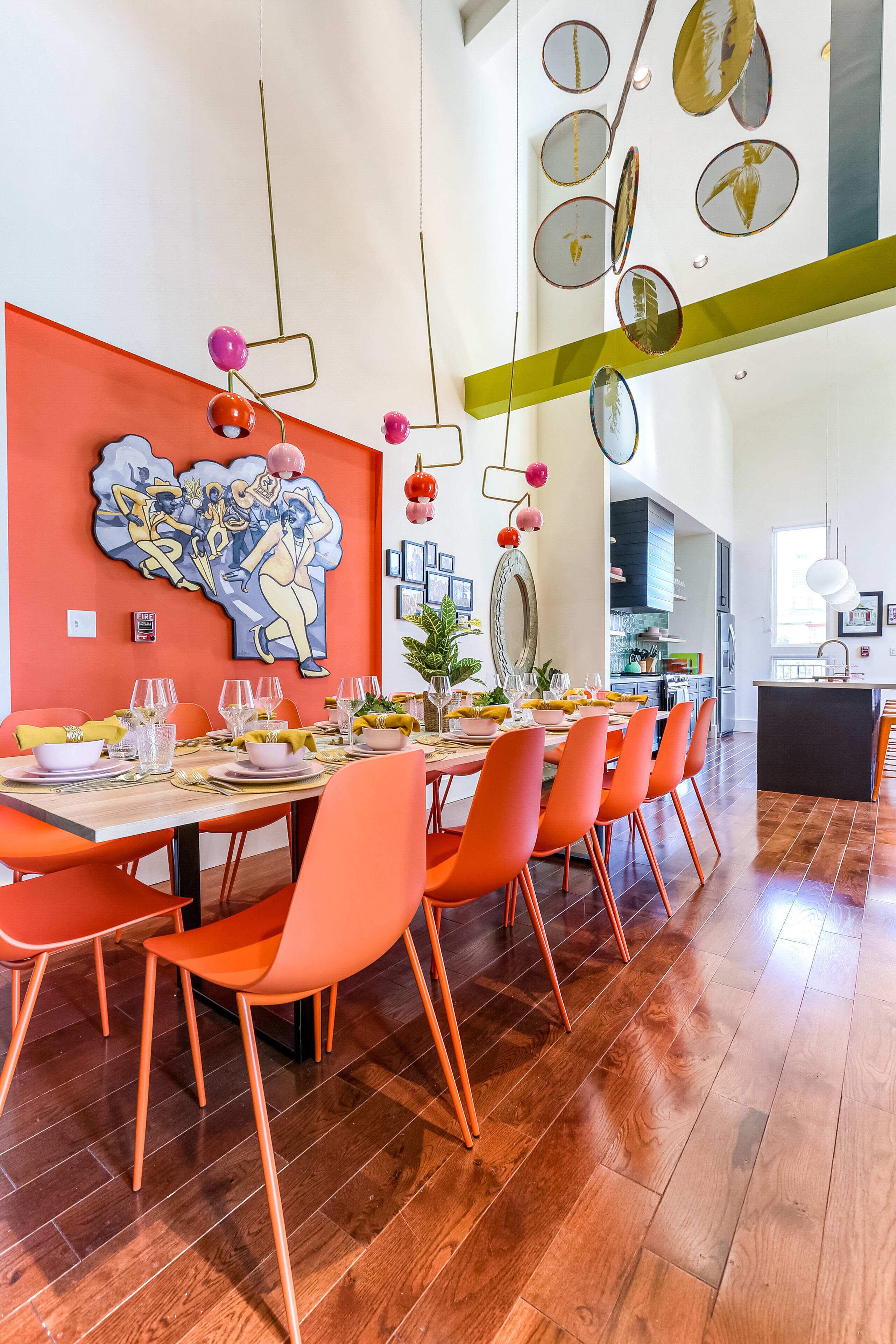 A dining area with orange chairs, a long table set for a meal, and a large abstract painting on the wall.