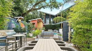Un patio exterior con terraza de madera, mobiliario de mimbre, una parrilla y una zona de piscina.