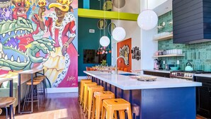 Una cocina moderna con barra, taburetes de madera y un mural colorido en la pared.