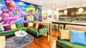 Un salon moderne avec un canapé vert, une table basse et une fresque murale aux couleurs vives.