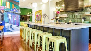 Une cuisine moderne dotée d’un îlot central, de tabourets de bar, de luminaires suspendus et d’un pare-feu vert.
