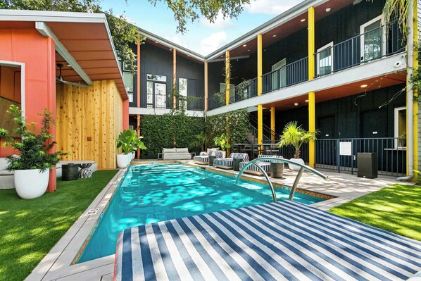Un espace piscine moderne doté d’une piscine rectangulaire, de chaises longues et d’une terrasse en bois.