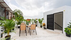 An outdoor patio area with a table and chairs, surrounded by potted plants and a white building with a black door. - Bamboo House (Santo Domingo)
