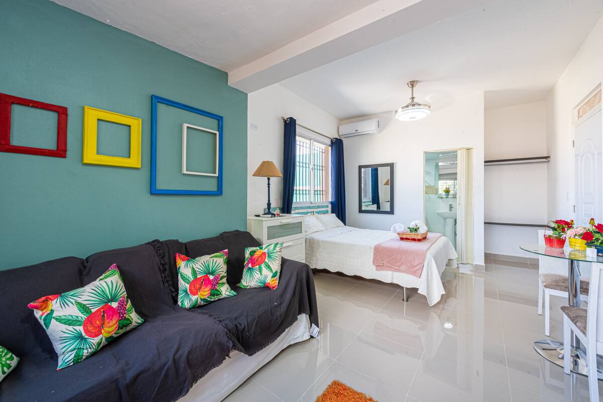 A modern room with a black sofa, a bed, a small table with flowers, and a mirror on the wall.