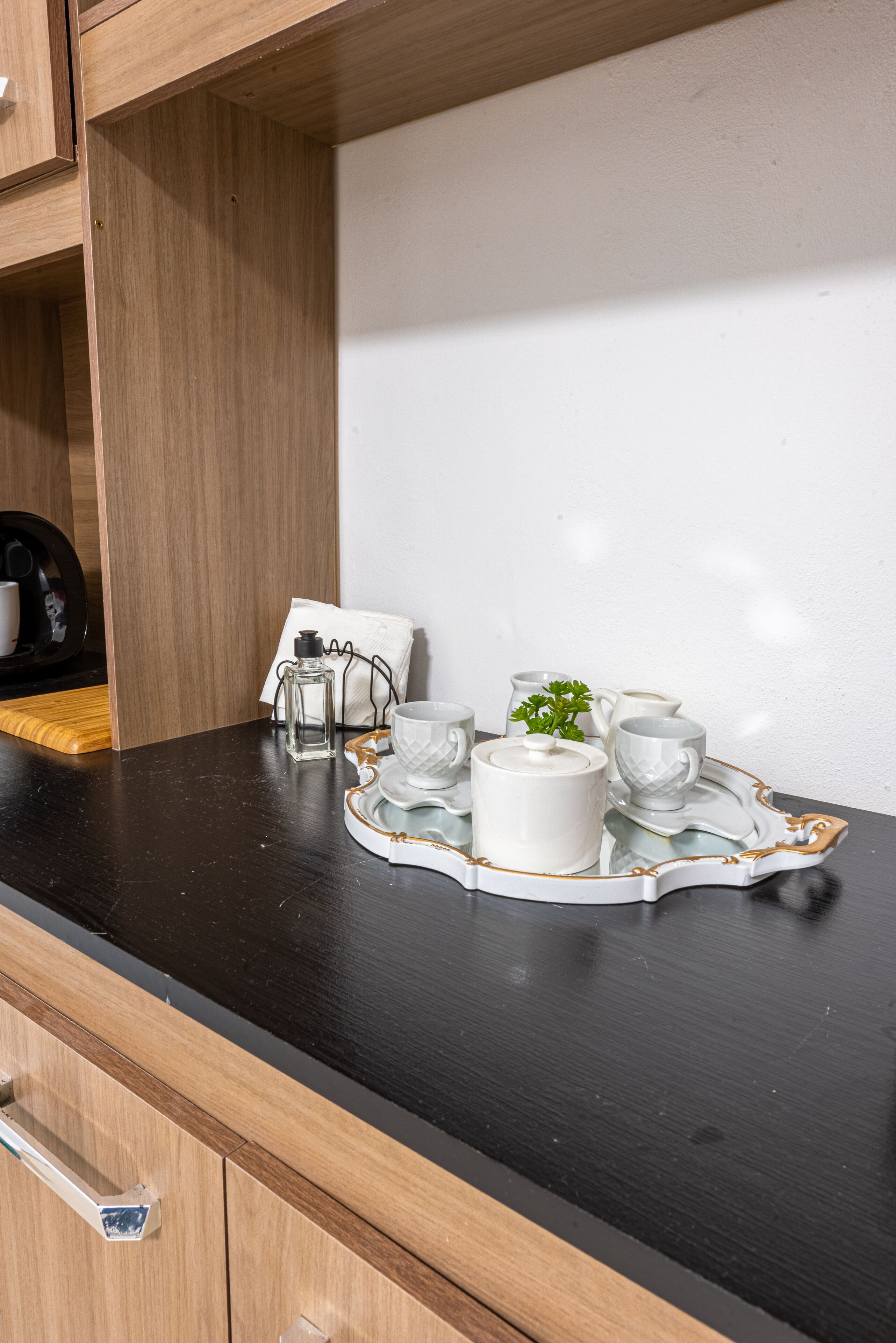 Una encimera de cocina con una bandeja que contiene tazas de cerámica blanca, una jarra y una planta pequeña.