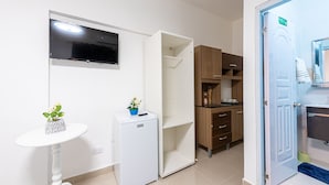 A compact room with a flat-screen TV mounted on the wall, a small white refrigerator, a table with a potted plant, and a wooden cabinet with open shelves. - Bamboo House (Santo Domingo)