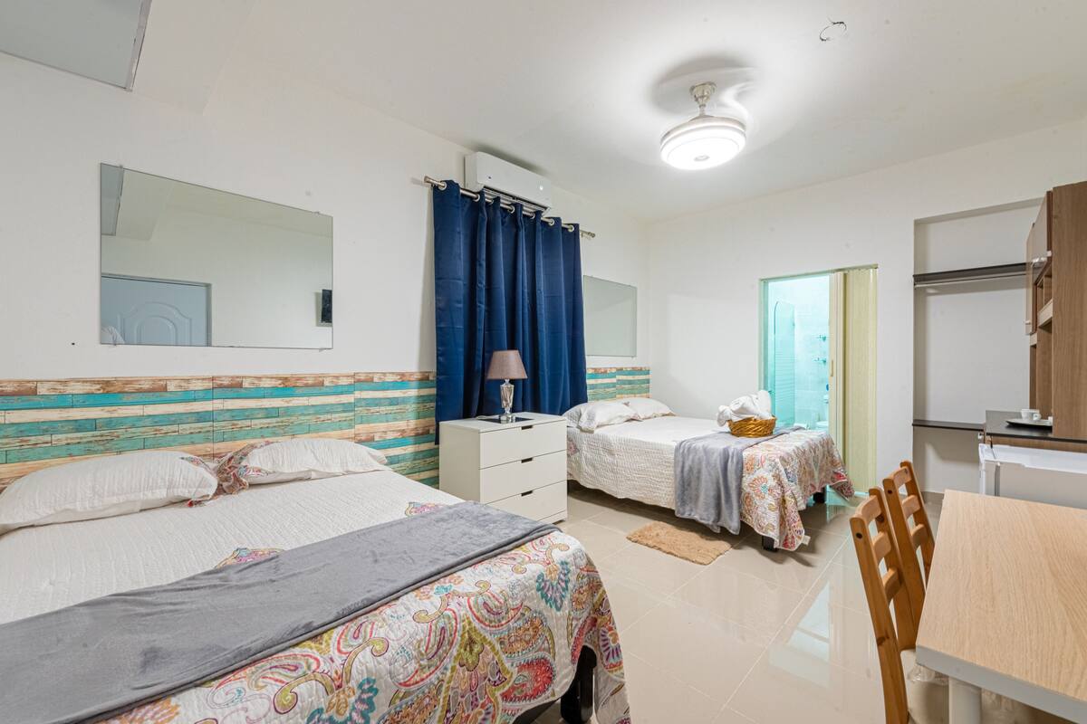 A bedroom with two beds, a bedside table with a lamp, a mirror, and a window with curtains.