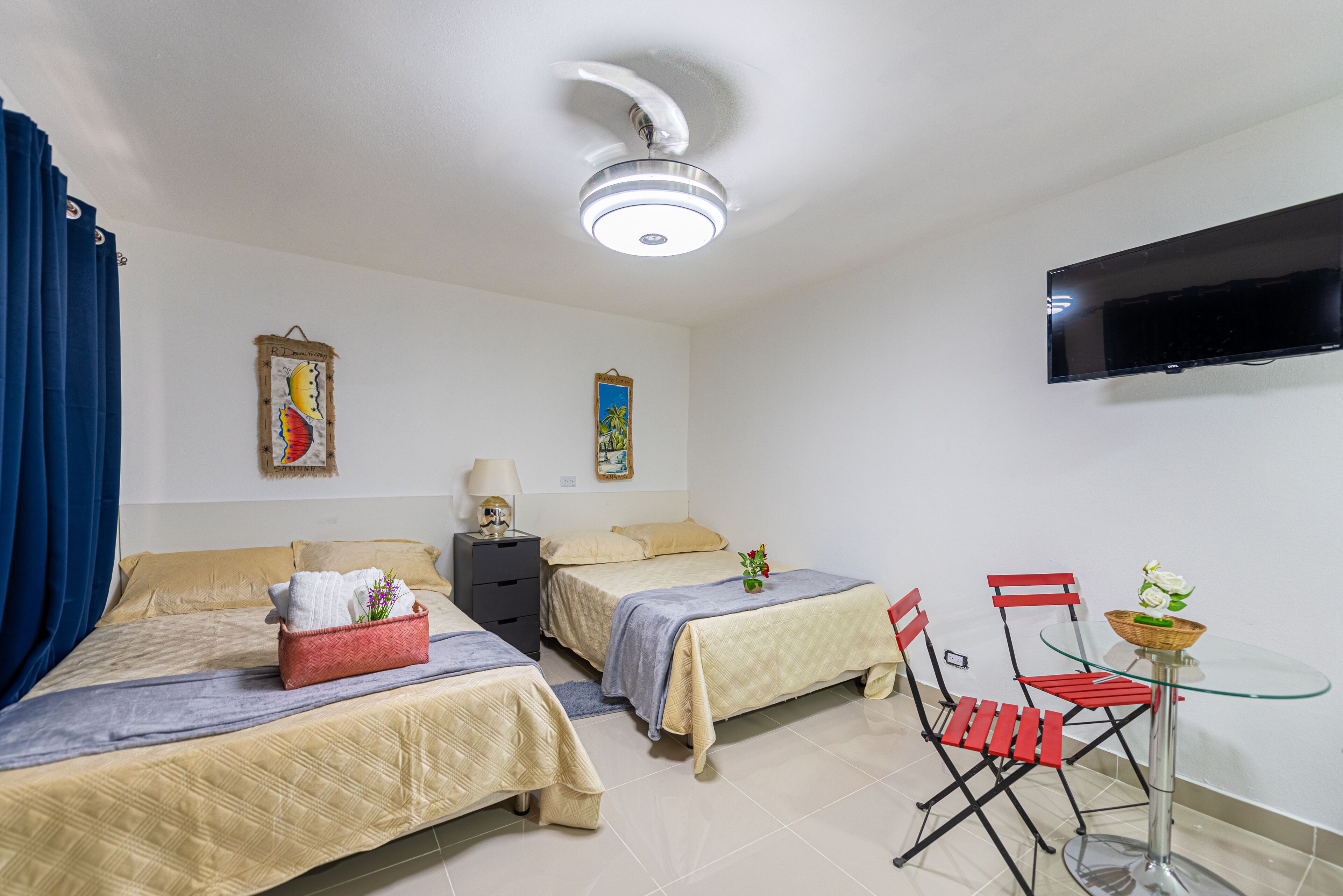 Hotellihuone, jossa on kaksi sänkyä, televisio, pöytä tuoleineen ja kattotuuletin.