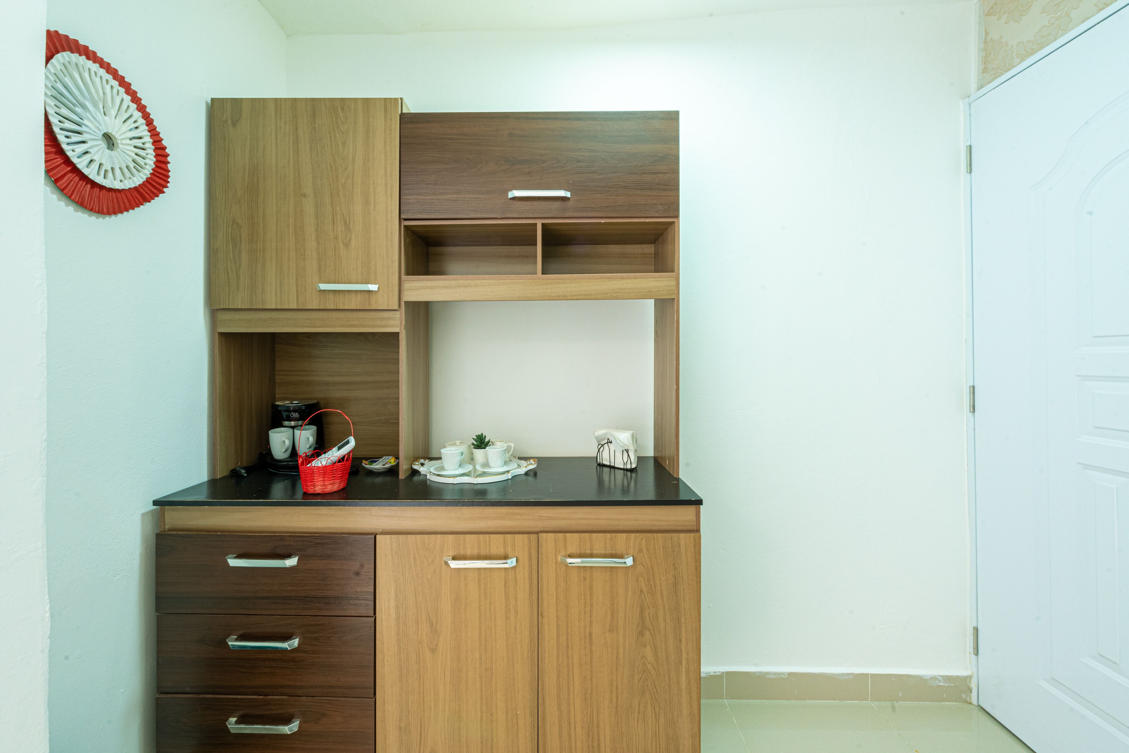 Une cuisine de taille réduite avec des meubles en bois, un plan de travail noir et un objet décoratif rouge accroché au mur.