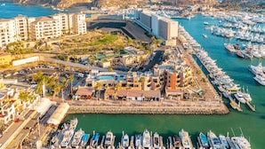 A marina with numerous boats docked, a large building with a curved structure, and a mountainous backdrop. - Newly Remodeled Condo In The Cabo Marina (Cabo San Lucas)