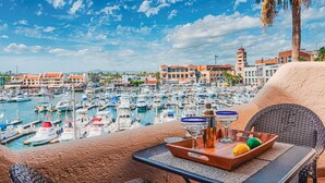 A marina with numerous boats docked, a view of the town, and a table with a tray of items. - Newly Remodeled Condo In The Cabo Marina (Cabo San Lucas)