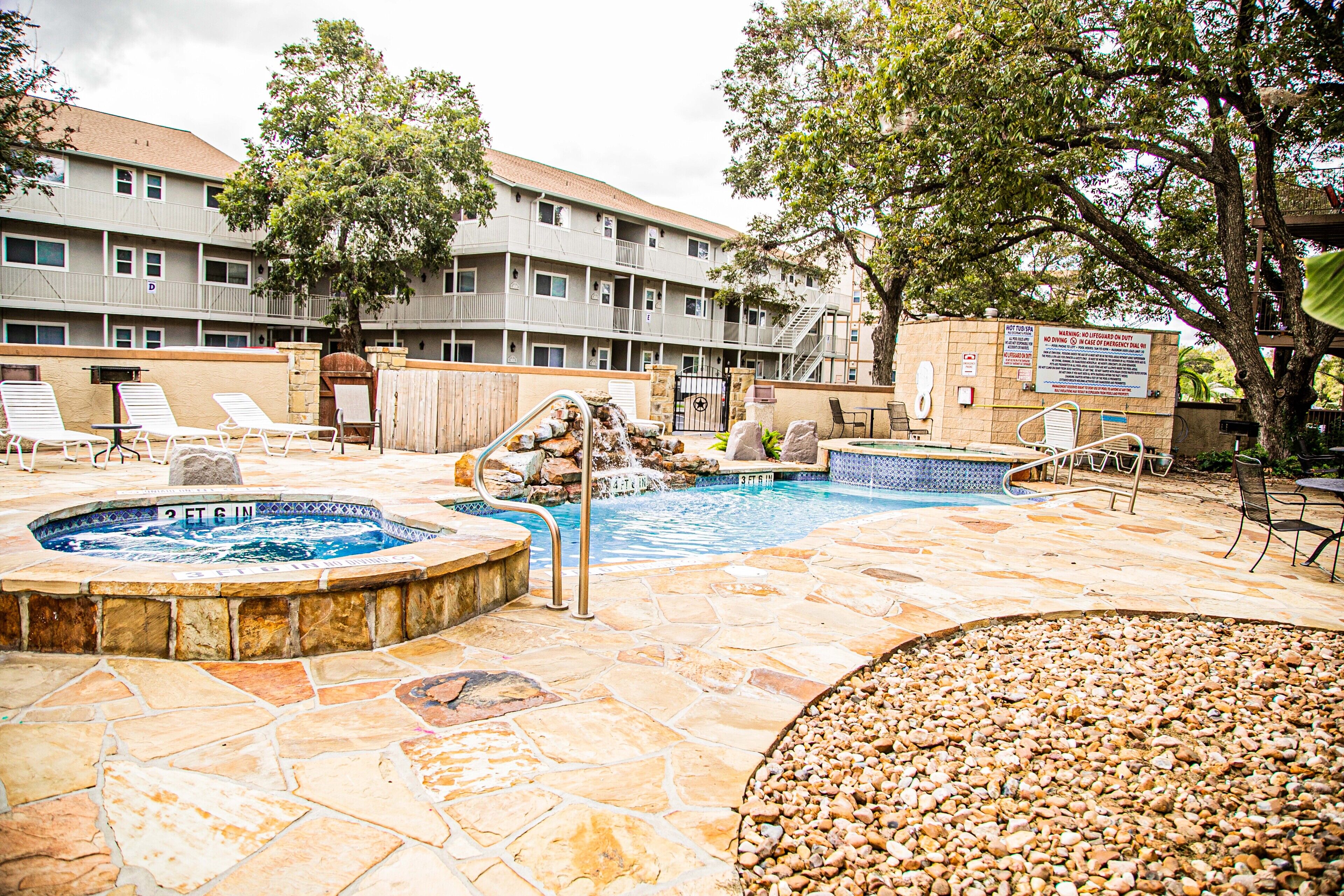 Zona de piscina hotelera con un jacuzzi, sillones reclinables y una terraza con baldosas de piedra.