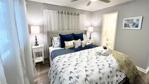 A bedroom with a bed, a ceiling fan, a nightstand, a lamp, and a framed picture on the wall.