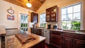 Une cuisine avec des armoires en bois, un comptoir en granit, un four encastré et une fenêtre décorée de motifs d’étoiles de mer.