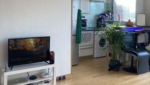 Een moderne keuken met een inbouwoven, magnetron en koffieapparaat. Er is een eethoek met een tafel en stoelen, en een televisie op een standaard.