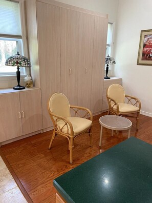 Quarto com duas cadeiras de vime, uma mesinha redonda e um armário com janela.
