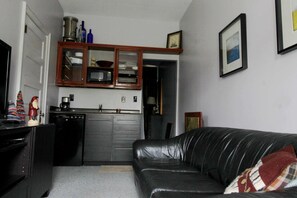 Um espaço compacto com cozinha compacta, um sofá de couro preto e um quadro na parede.