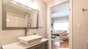 A modern bathroom with a large mirror, a vessel sink, and a shower area. - The Lilly Pad • Charming 1BR • Walk to Sylvan Beach (Sylvan Beach)