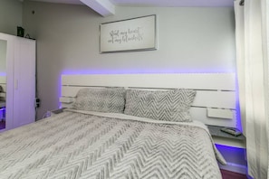 A bedroom with a bed, a headboard, a wall-mounted sign, and a door.