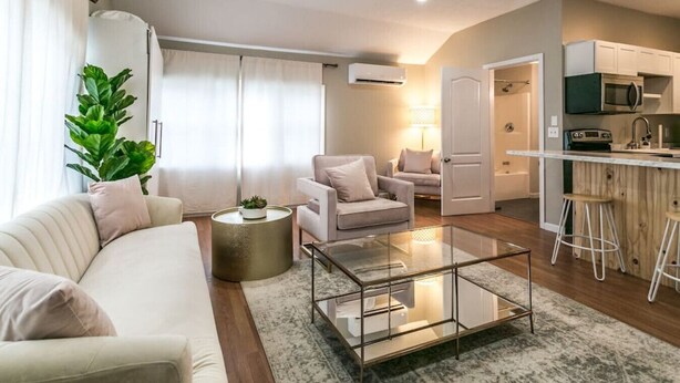 A modern living room with a sofa, a coffee table, and a kitchen area with a microwave and stools. - The Lilly Pad • Charming 1BR • Walk to Sylvan Beach (Sylvan Beach)