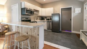 A modern kitchen with white cabinets, stainless steel appliances, and a bar area with stools. - The Lilly Pad • Charming 1BR • Walk to Sylvan Beach (Sylvan Beach)