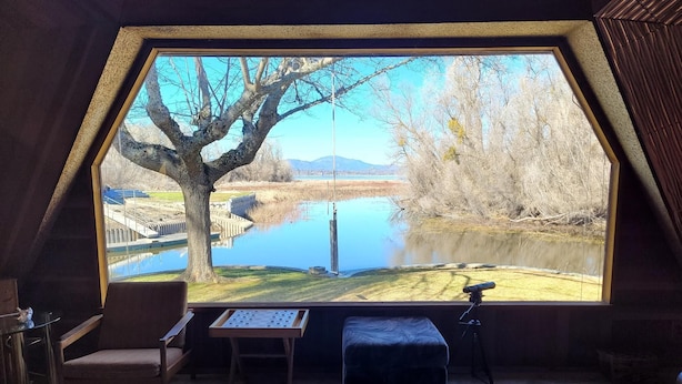 A room with a large window overlooking a lake, a table, and a chair. - Picturesque sunset views  perfect for couples, families and fishermen (Lakeport)